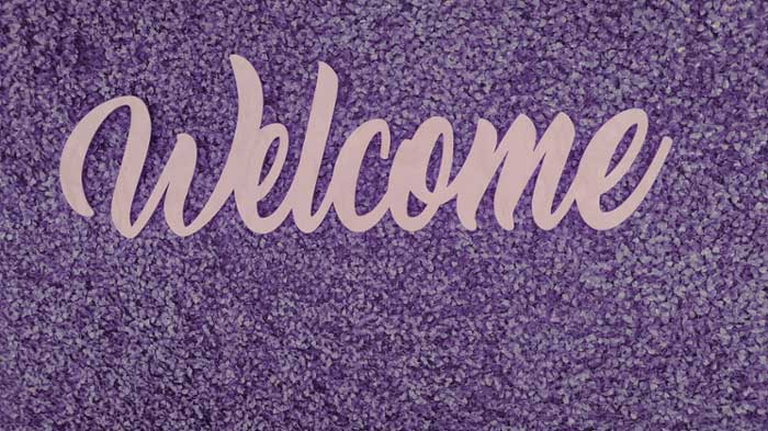 Sign that reads, "welcome" hung upon a hedge wall. 